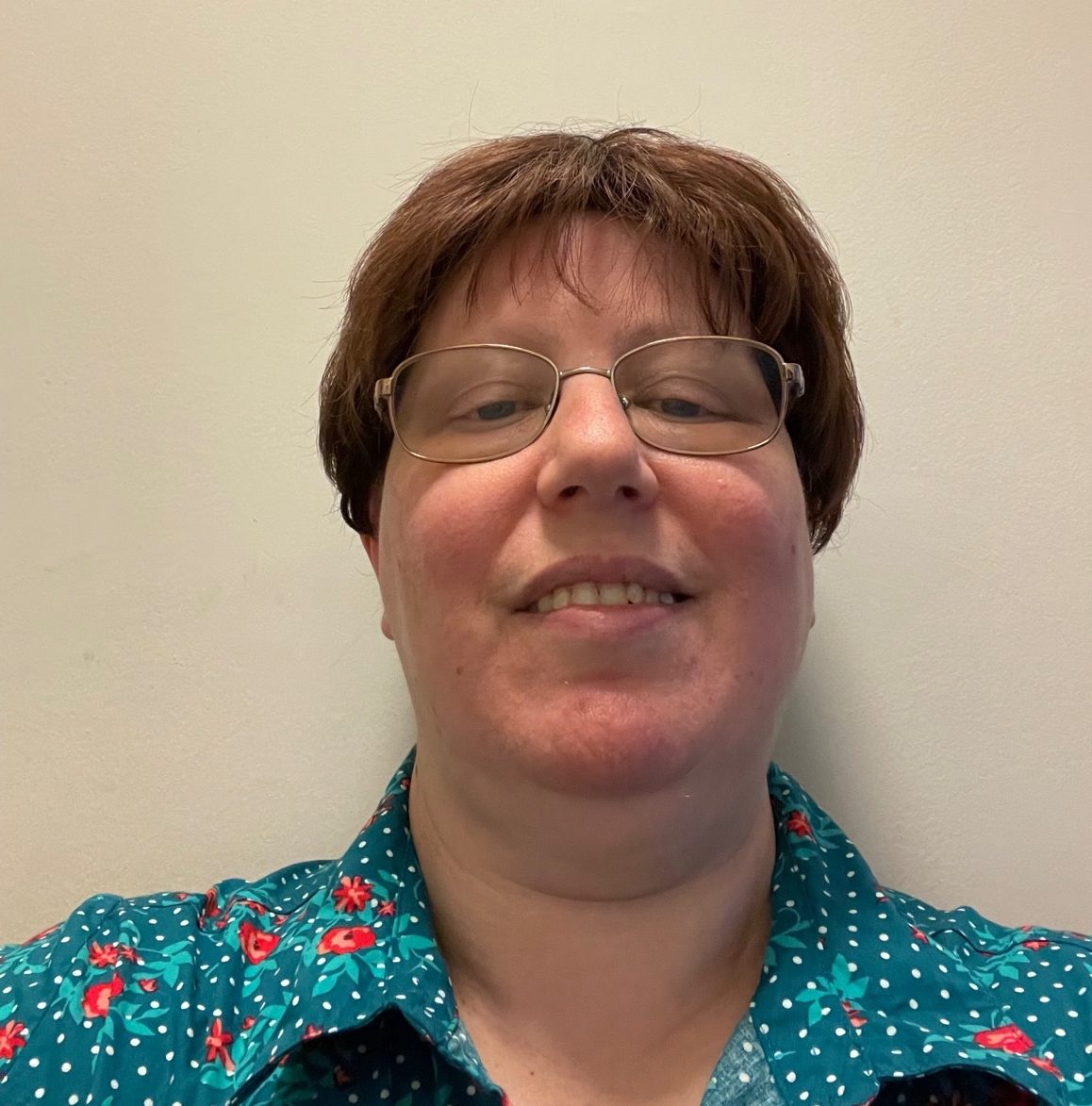 A woman with short hair and glasses smiles at the camera.