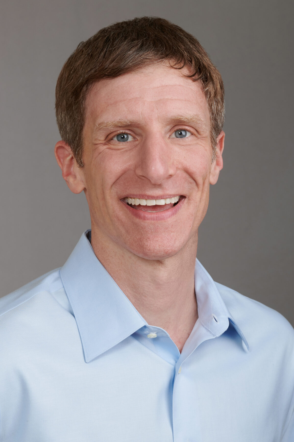 Man with short hair and a blue shirt smiles at camera.