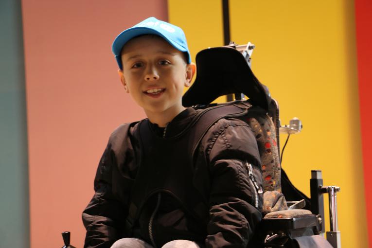 Picture of an 11-year-old child wearing a baseball cap and seated in a power chair.