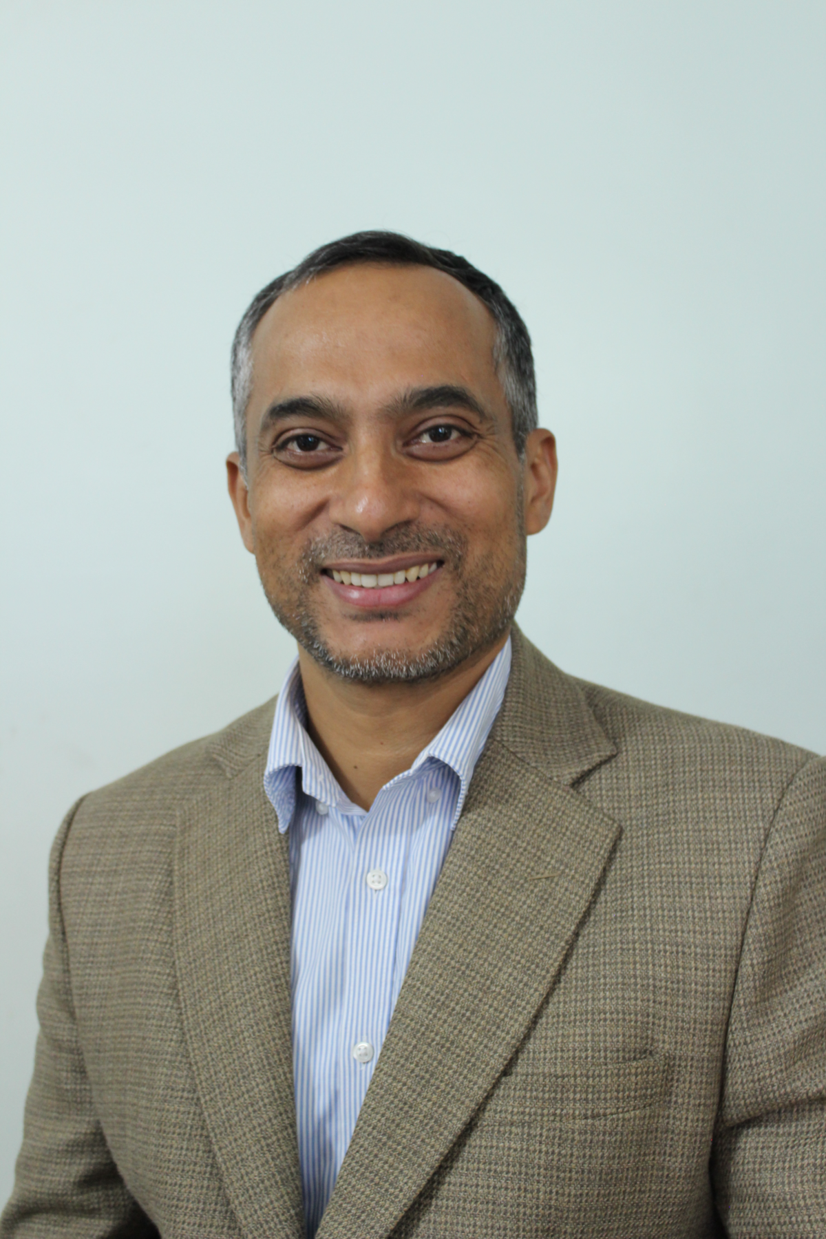 Man with short hair in a suit jacket smiles at camera.