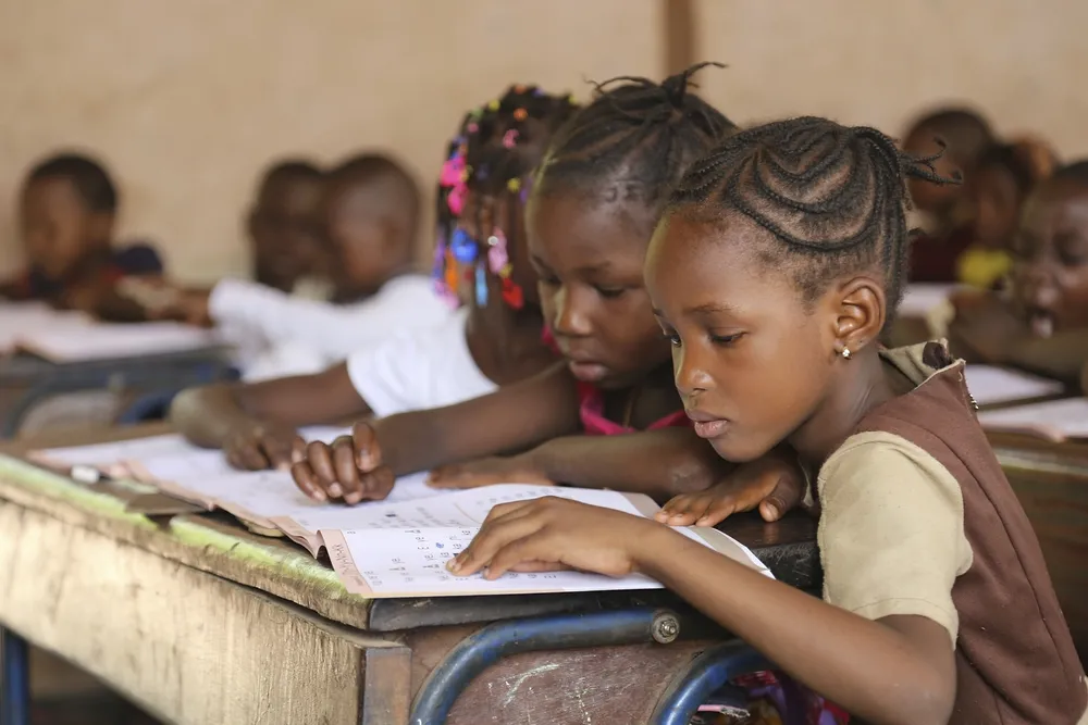School children share desks, each silently reading a school book.