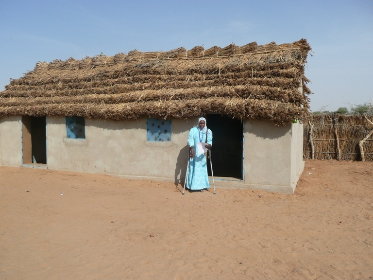 woman with a disability standing in from of her house in Darfur